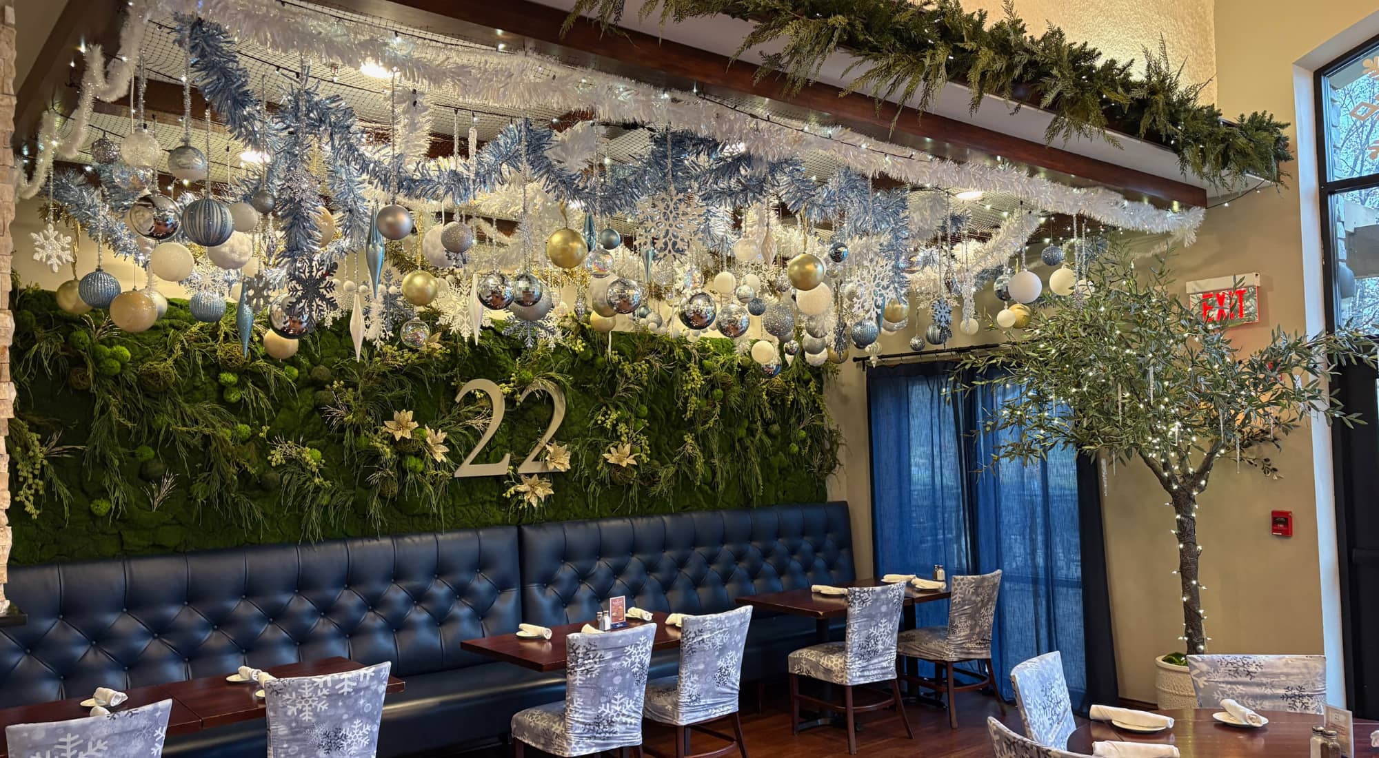 Festively decorated restaurant interior with blue and silver ornaments, greenery, and a table number 22.